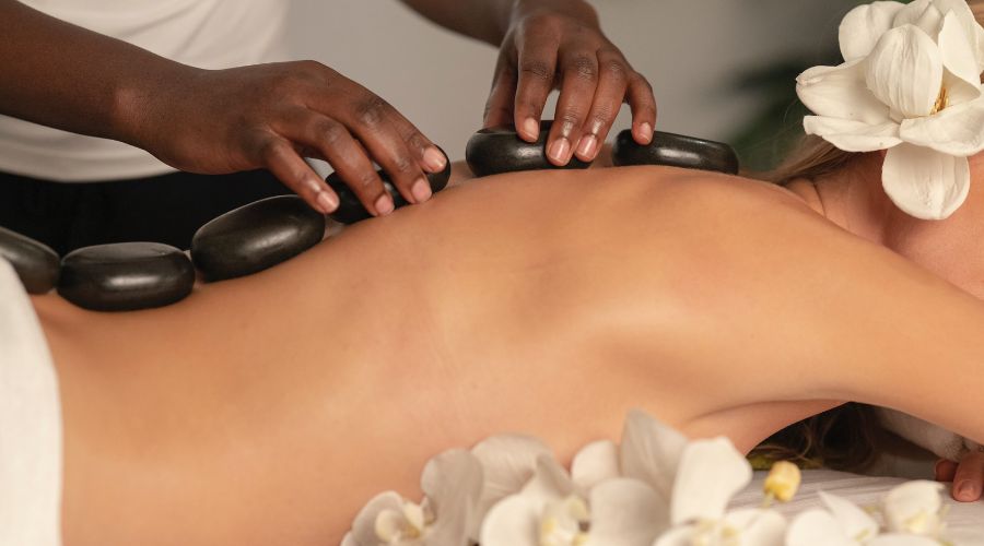 A massage therapist applies hot stones to someone's back.